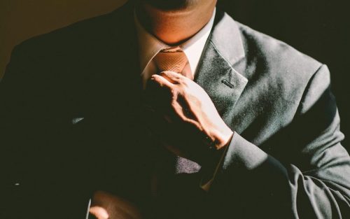 man adjusting tie in black suit, image used for Lisa Laporte blog on successful tech entrepreneurs